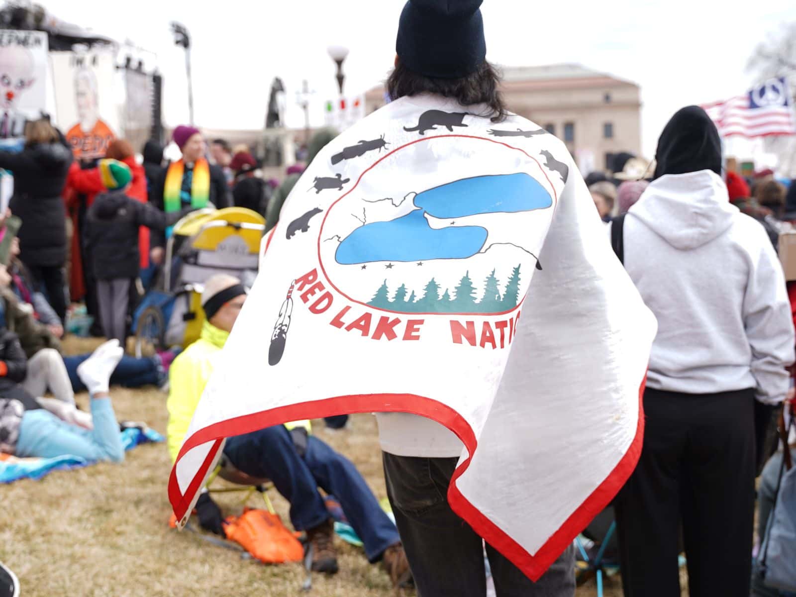 A “No Kings” participant walks through the crowd wearing a Red Lake Nation tribal flag at the Minnesota State Capitol grounds.