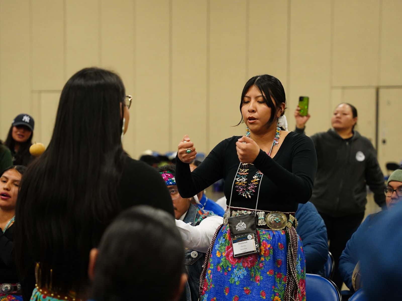 A hand game competitor from Diné College is hiding marked items given to her by her team caption. The opposing team from Navajo Technical University must guess where the marked items are in her hands.