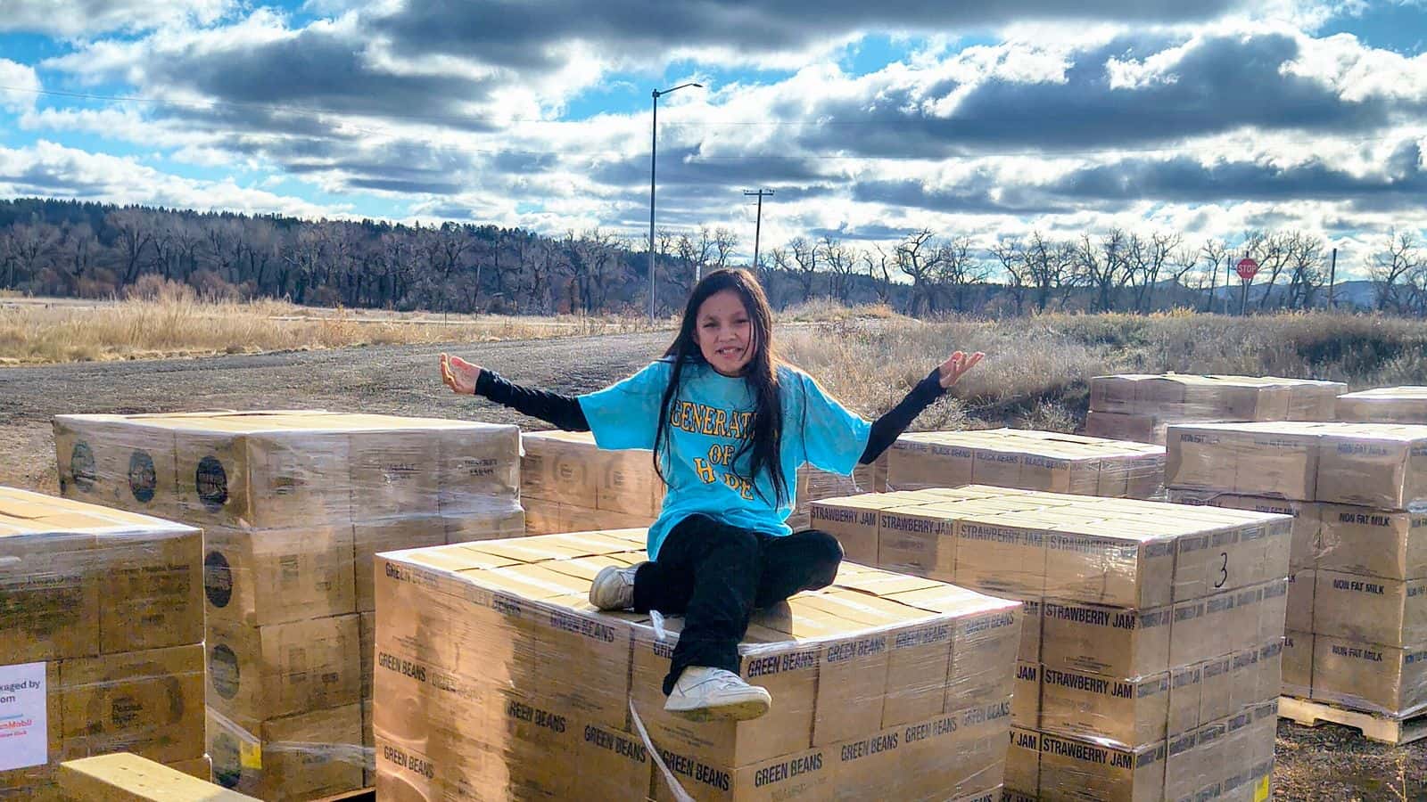 Anna Fishinghawk sits on top of boxes of food donated by the Church of Jesus Christ of Latter-day Saints to the Generations for Hope food drive, Northern Cheyenne Reservation, Montana, Tuesday, Nov. 25, 2025. Volunteers distributed 512 boxes to people living on the Northern Cheyenne Reservation. (Generations for Hope/Tonah Fishinghawk-Chavez)