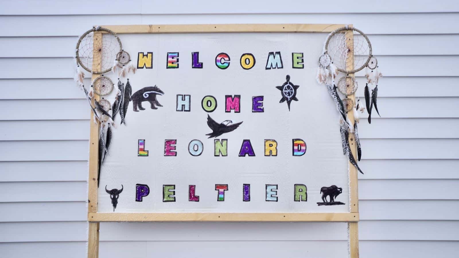 A "Welcome Home" sign is displayed for Leonard Peltier in Belcourt, N.D. 