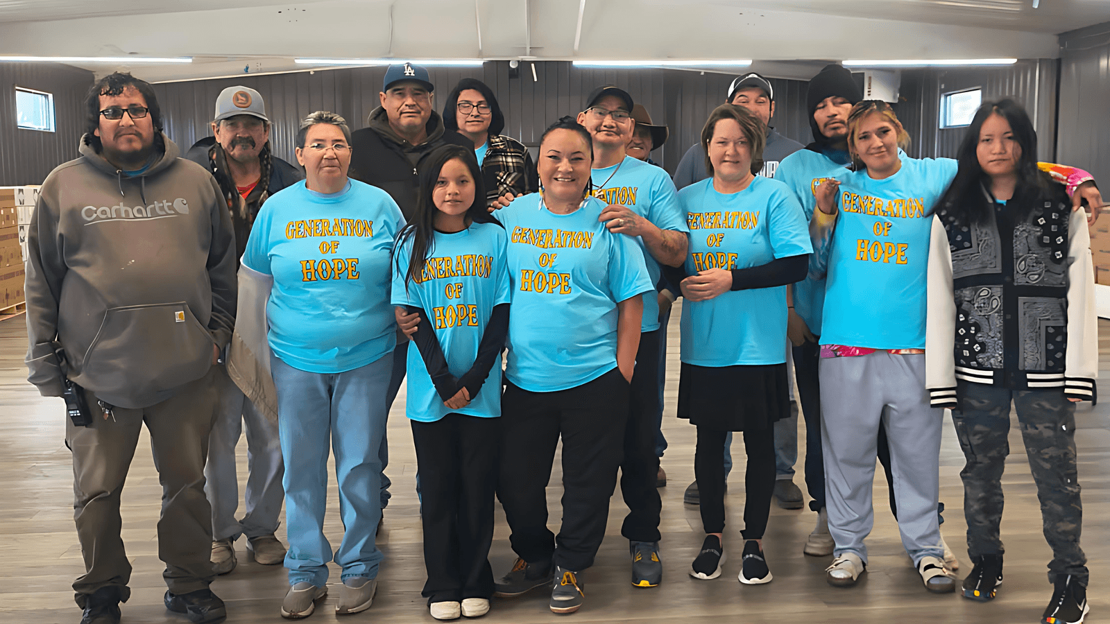 With her daughter Anna to her right and her husband, Carlos Chavez, behind her, Tonah Fishinghawk-Chavez (middle) stands among community volunteers and boxes of food, Ashland, Montana, Tuesday, Nov. 25, 2025. (Generations for Hope/Charlene Robinson)