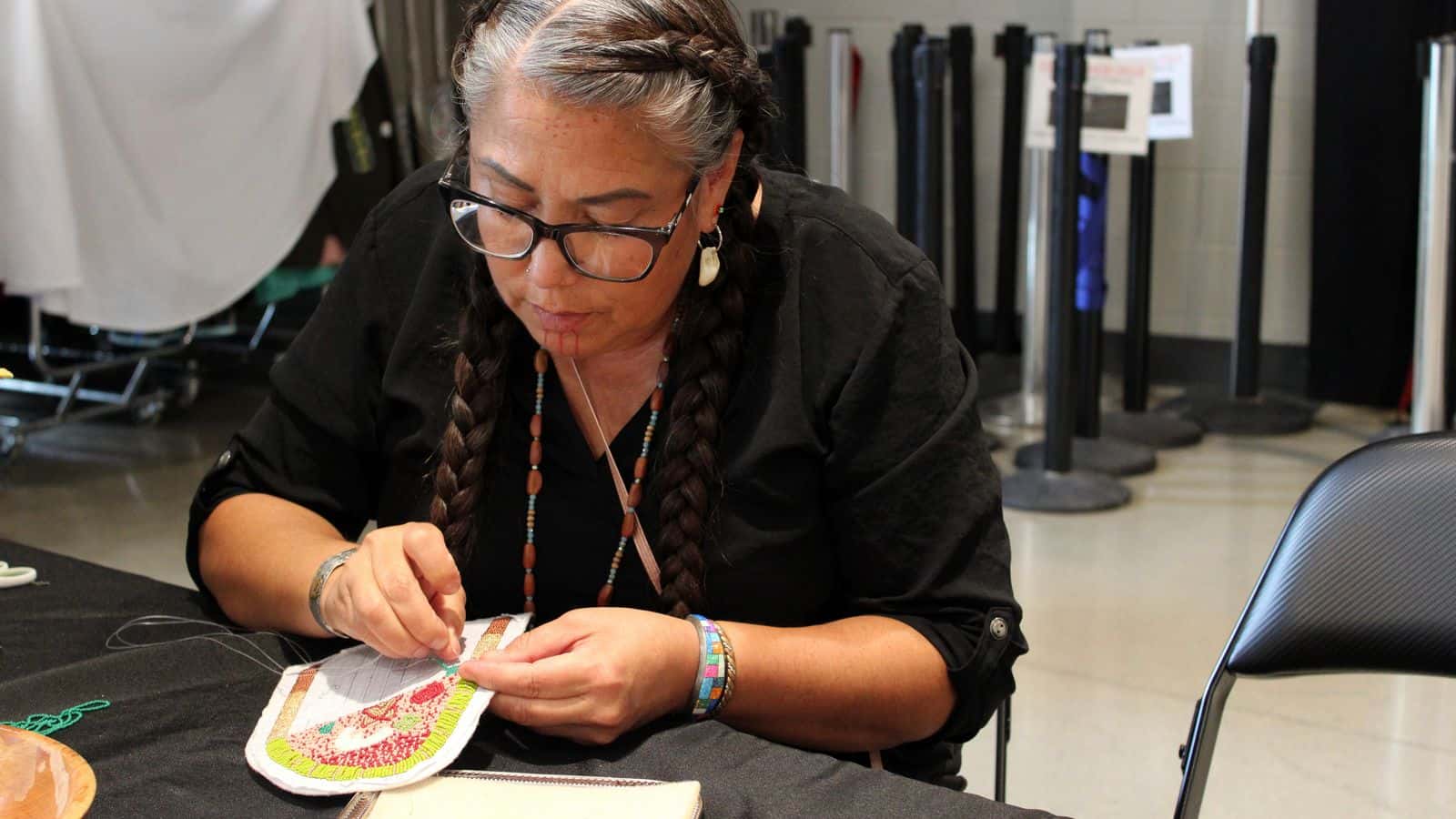 Kelly Hosie beads a piece of regalia at the Four Bears Casino. She sold her beadwork and baked items at a booth during the alterNATIVE Medicine Symposium and attended sessions to learn more about medical marijuana, July 29, 2025. (Photo credit: Gabrielle Nelson)