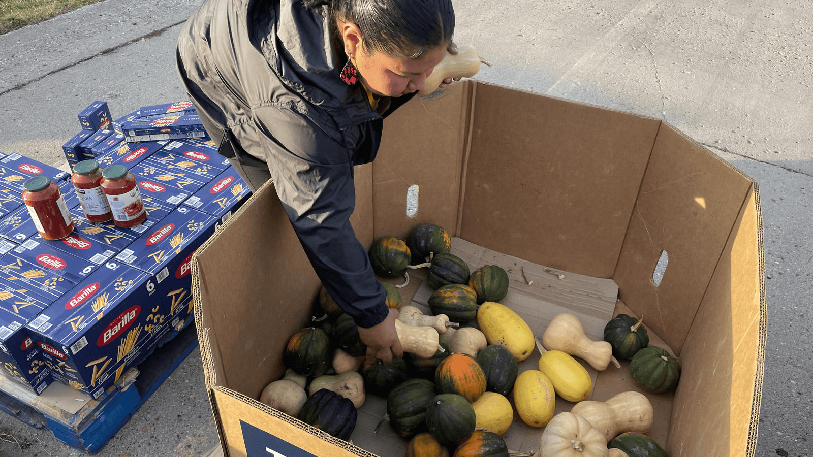 Volunteer Melanie Moniz, an enrolled citizen of the Mandan, Hidatsa and Arikara Nation, grabs squash to give to people at the food distribution event at Sacred Pipe Resource Center in Bismarck, North Dakota, Wednesday, Nov. 12, 2025. (Buffalo’s Fire/Gabrielle Nelson)
