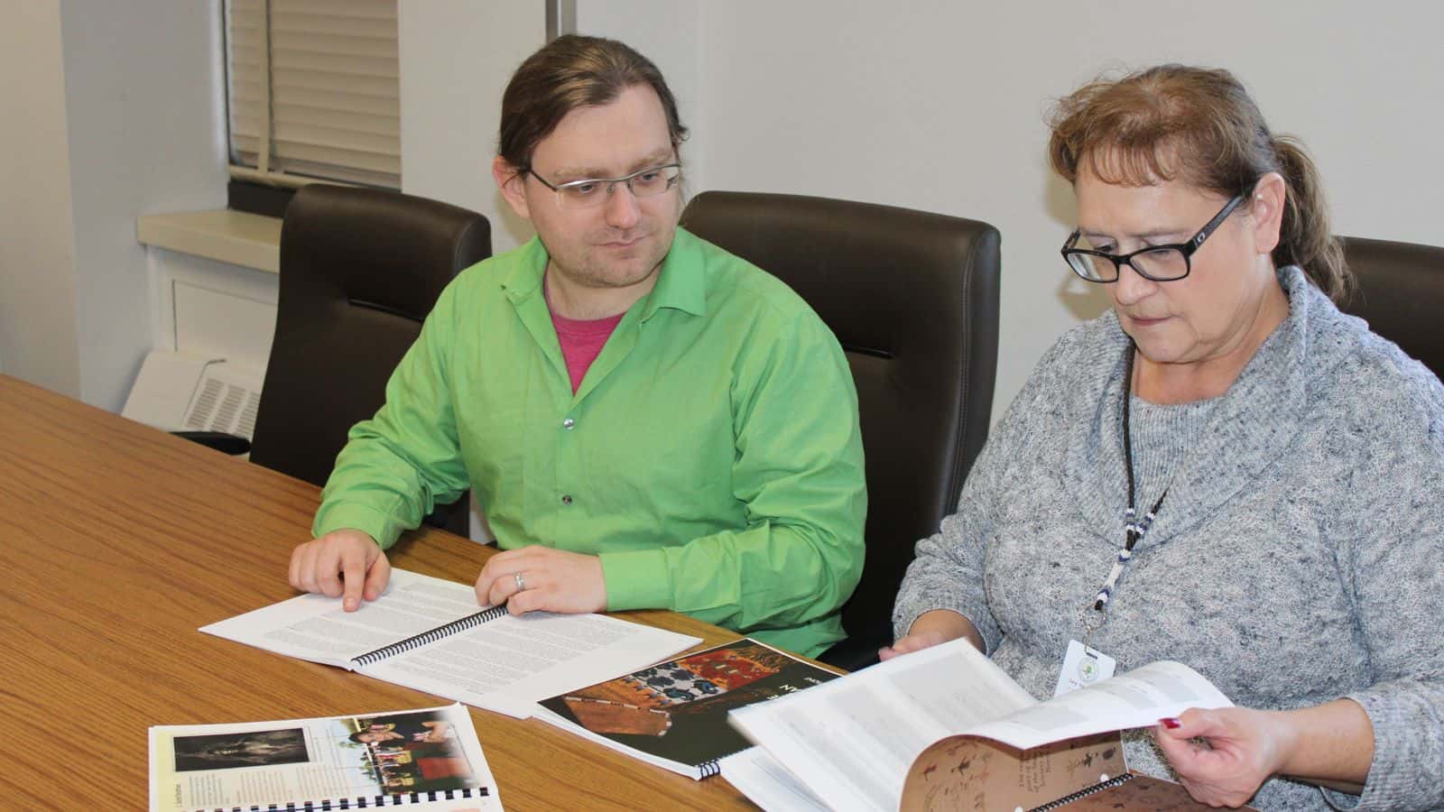 Lucy Fredericks and Nick Asbury peer through the original set of tribal curriculum guides published from 1997 to 2002 to access what other information could be included in the updated versions on Dec. 18. Photo credit/ Adrianna Adame