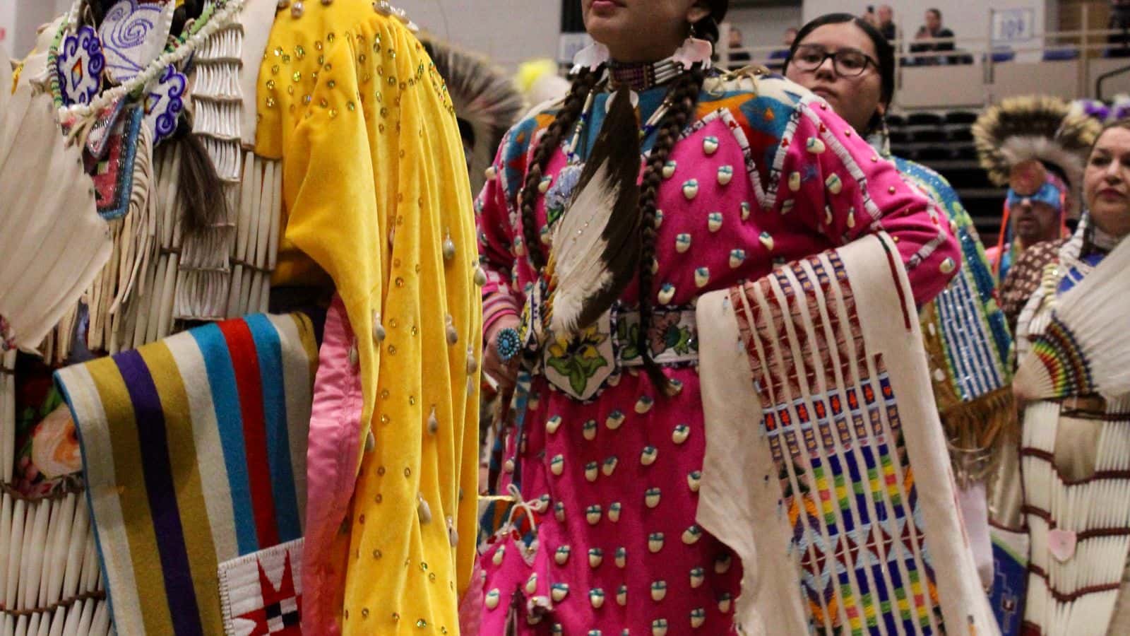 Cyra Plainfeather, MHA Nation and Crow, dances in a pink dress with a shawl and eagle feather fan in line of women traditional dancers during the second grand entry, Bismarck Event Center, North Dakota