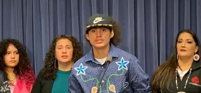 Nimkii Curley, Diné and Ojibwe, center, speaks at a press conference at the Illinois State Capitol on Wednesday, Nov. 16, 2022, at a Native American Summit aimed at drawing attention to Indigenous issues in the state. Curley was not allowed to participate in his graduation ceremony in May 2022 because he had an eagle feather on his graduation cap. Curley's mother, Megan Bang, Ojibwe, second from right in green shirt, also spoke about her son's experience and the harmful effects of Native mascots. The summit was organized by the Chicago American Indian Community Collaborative (Photo by Amelia Schafer for ICT)