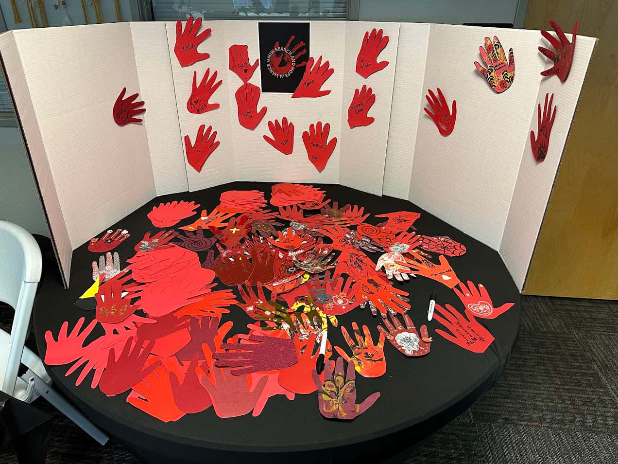 A table display invites visitors to write down the names of people they are mourning or missing on red paper hands.