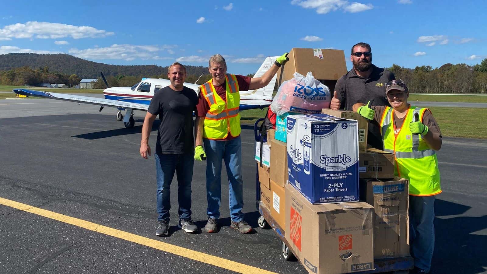 Casey Veil (left, black shirt) and Treven Iverson (right, sunglasses) of Jamestown pose with volunteers and the supplies they flew into a distribution point in Jefferson, N.C. on Oct. 5. Contributed by Veil. 