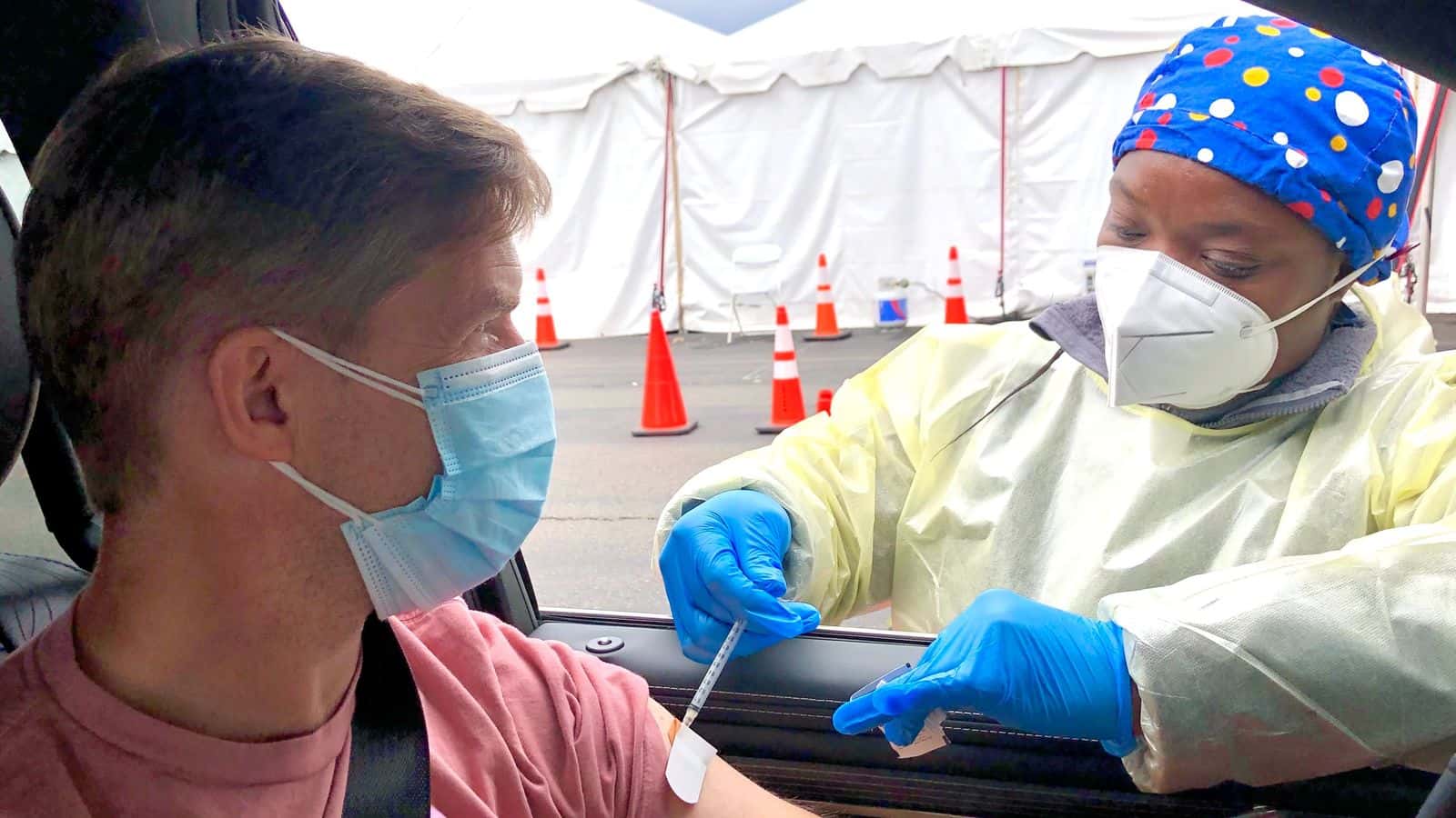 A medical worker administers a COVID vaccine to a person in their car.