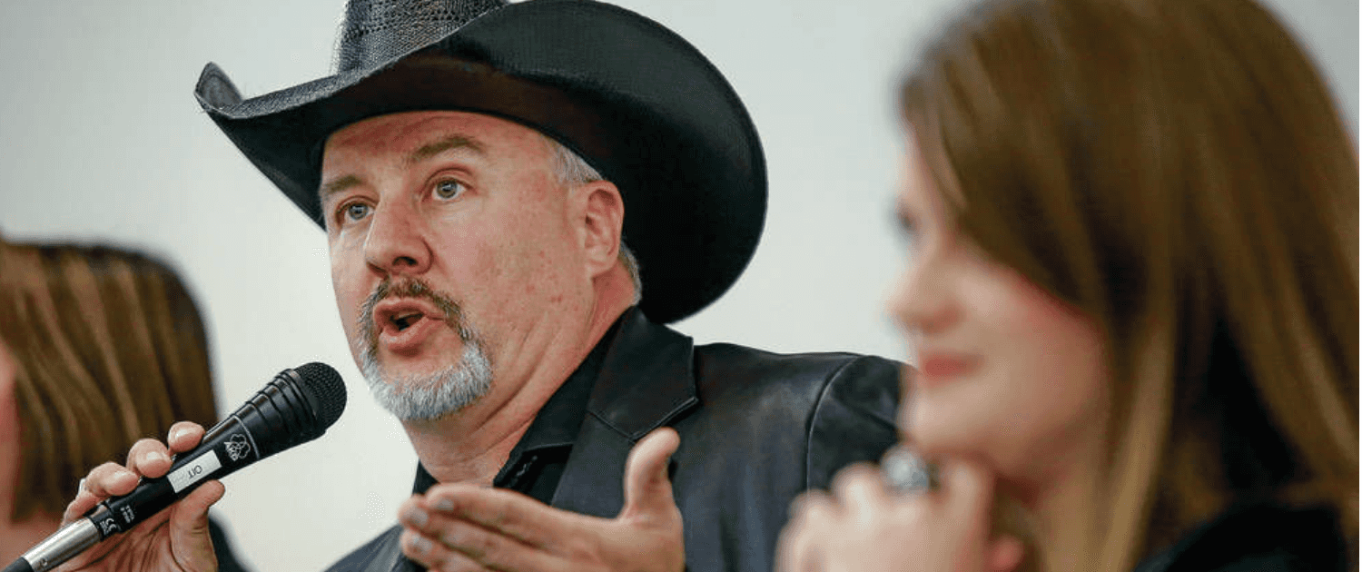 Gavin Clarkson native american man with black cowboy had and black jacket speaking into microphone