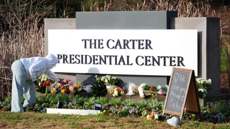 Christine Mason, of Atlanta, places flowers at the entrance to The Jimmy Carter Presidential Center in Atlanta, Georgia, on Monday, Dec. 30, 2024. Formr President Jimmy Carter died Sunday at his home in Plains, Georgia, at the age of 100. (AP Photo/John Bazemore )