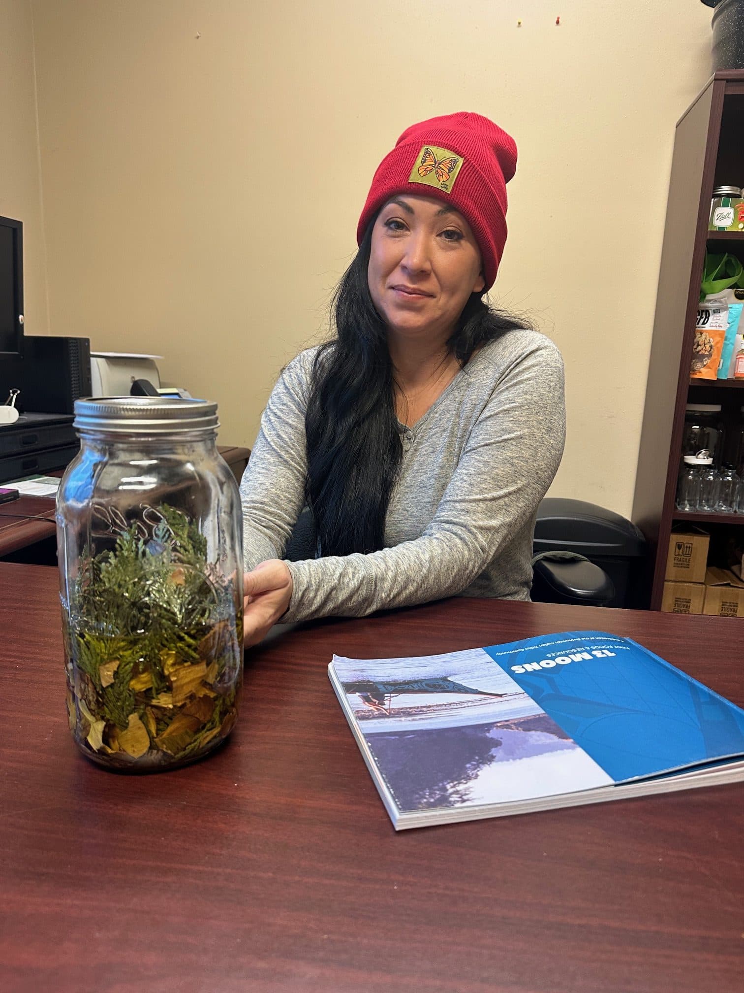 Beth Willup, the Swinomish Tribe’s environmental health program coordinator, sits in her office with a jar of preserved medicinal plants on her desk, January 2025. Making healing salves from medicinal plants is an activity during the Moon of the Salmonberry.