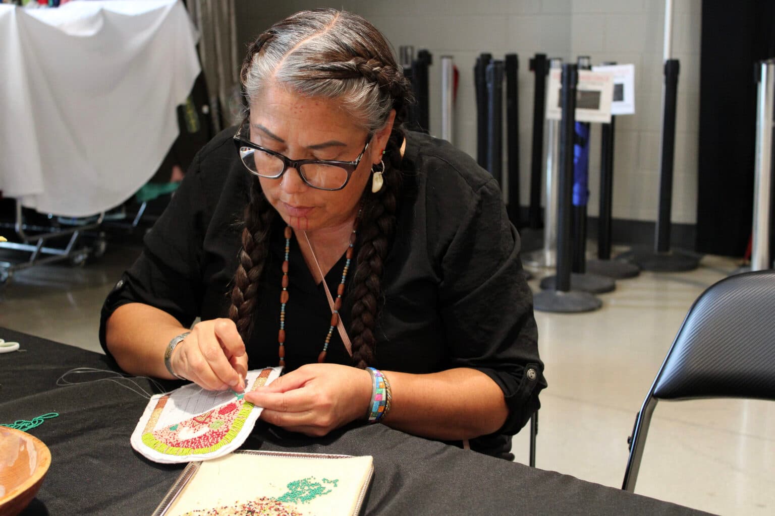 Kelly Hosie beads a piece of regalia at the Four Bears Casino. She sold her beadwork and baked items at a booth during the alterNATIVE Medicine Symposium and attended sessions to learn more about medical marijuana, July 29, 2025. (Photo credit: Gabrielle Nelson)