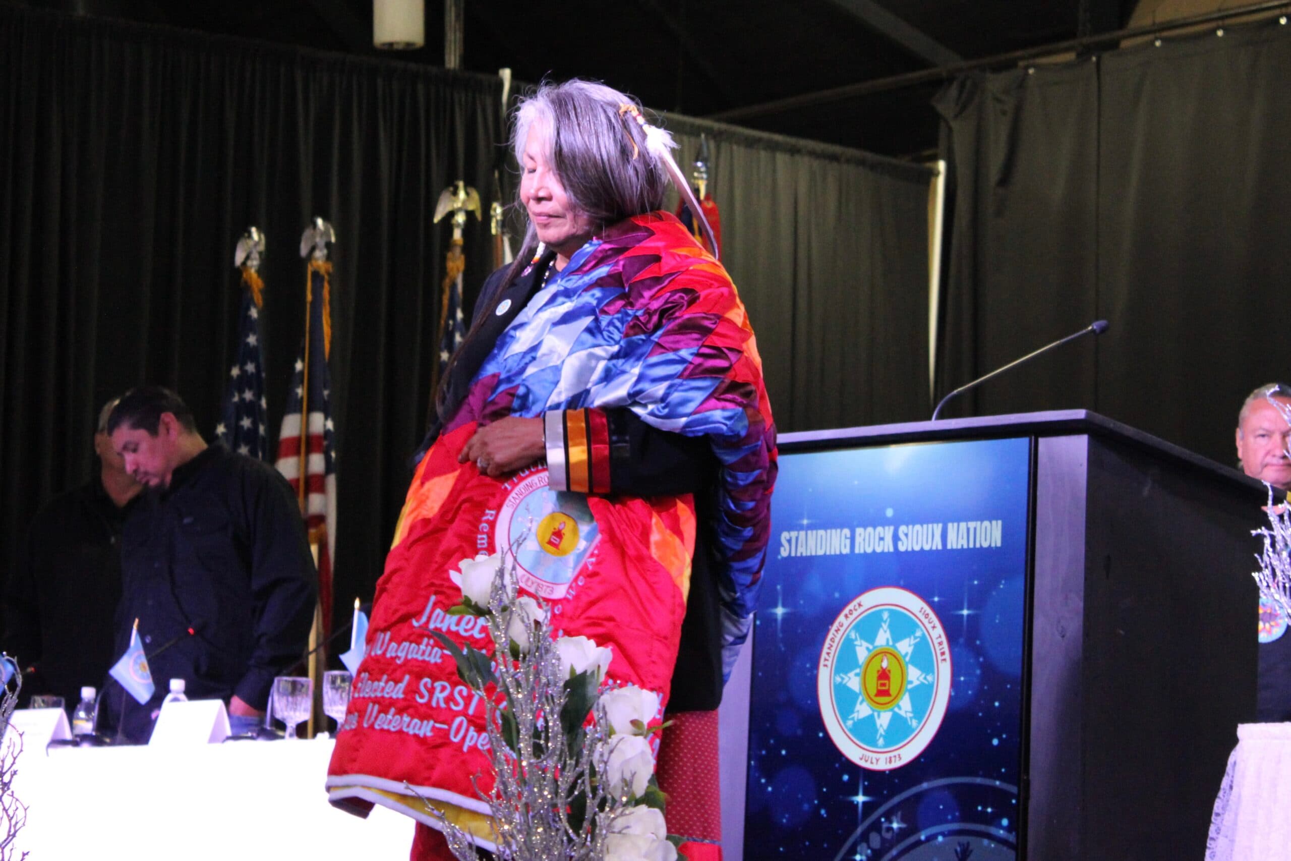 Outgoing Chairwoman Janet Alkire stands on stage with a gifted eagle feather and star quilt at the 2025 Standing Rock Sioux Tribe Inauguration at the Prairie Knights Casino &amp; Resort. Alkire served as chair from 2021 to 2025 and was the first elected woman to hold the position, Fort Yates, North Dakota, Wednesday, Oct. 8, 2025.