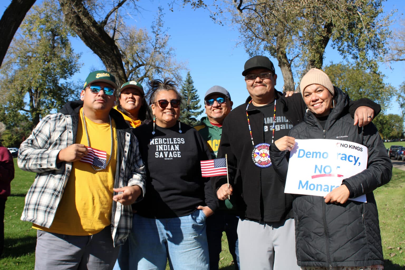 Standing Rock Sioux Tribe citizens Peter Taken Alive, Summer Swimmer, Juliana White Bull, Crawford Taken Alive and Jonas Taken Alive and Umonhon Tribe of Nebraska citizen Lillian Taken Alive, stand together on the lawn of the state capitol at the “No Kings” rally. White Bull wore a shirt that said “Merciless Indian Savage,” Bismarck, North Dakota, Saturday, Oct. 18, 2025. (Buffalo’s Fire/Gabrielle Nelson)
