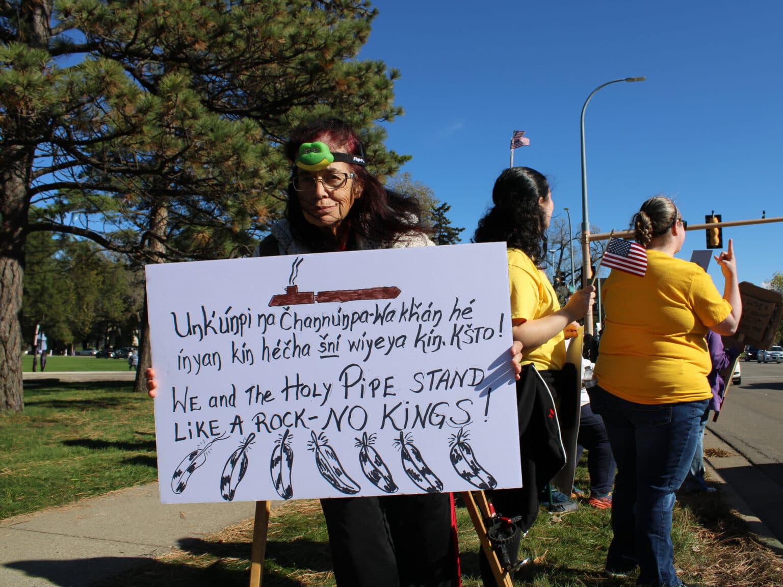 At the “No Kings” rally, Carel Two-Eagle (Lakota), a Pipe Carrier and Sundancer, holds a sign that reads in Lakota and English, “We and the Holy Pipe stand like a rock — NO KINGS!” Bismarck, North Dakota, Saturday, Oct. 18, 2025. (Buffalo’s Fire/Gabrielle Nelson)