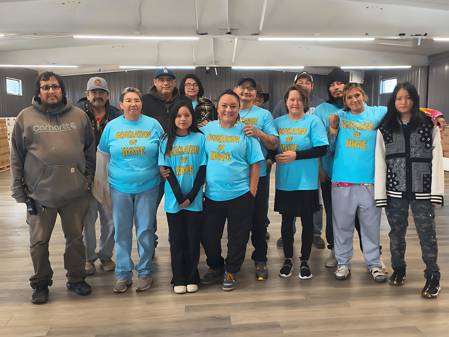 With her daughter Anna to her right and her husband, Carlos Chavez, behind her, Tonah Fishinghawk-Chavez (middle) stands among community volunteers and boxes of food, Ashland, Montana, Tuesday, Nov. 25, 2025. (Generations for Hope/Charlene Robinson)