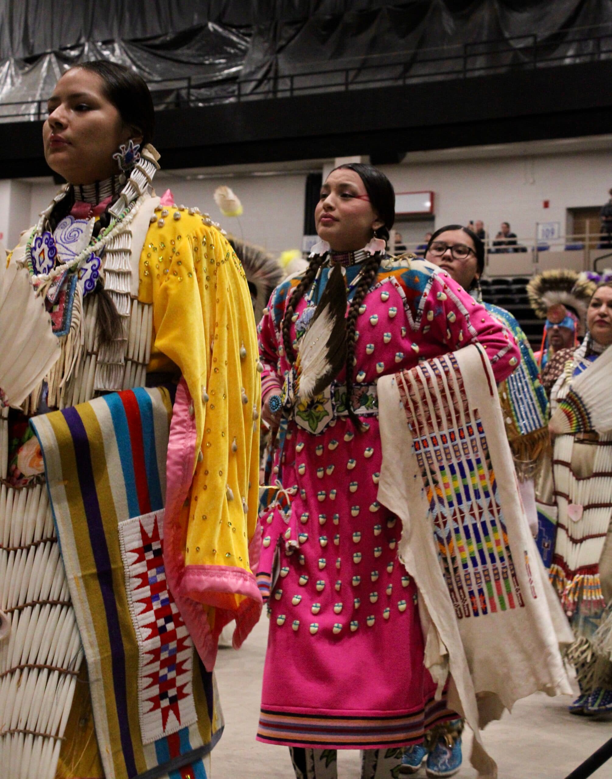 Cyra Plainfeather, MHA Nation and Crow, dances in a pink dress with a shawl and eagle feather fan in line of women traditional dancers during the second grand entry, Bismarck Event Center, North Dakota