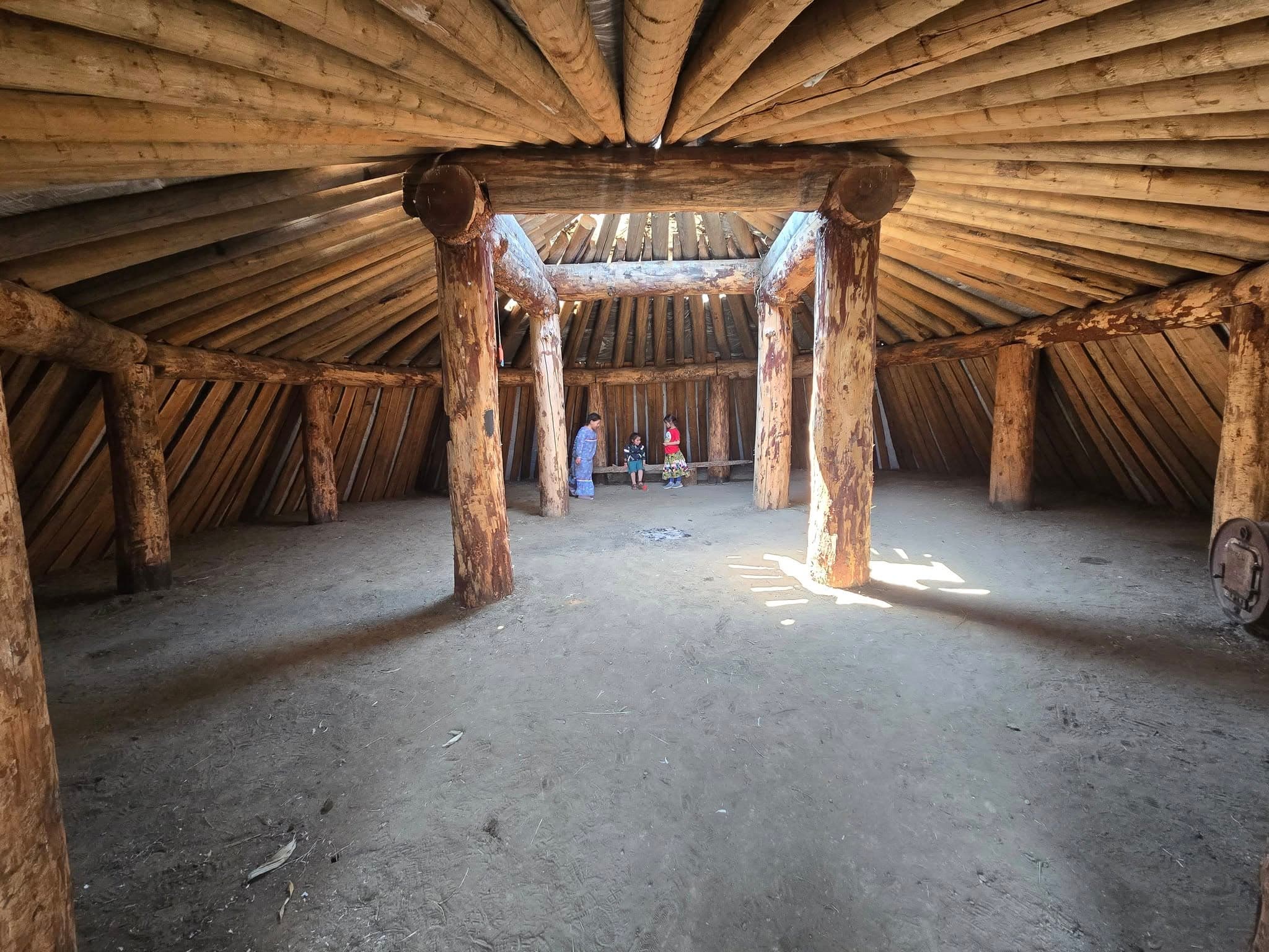 Three kids play inside one of the earthlodges built by Mní Wičhóni Nakíčižiŋ Wóuŋspe students, Bear Soldier, South Dakota, 2021.