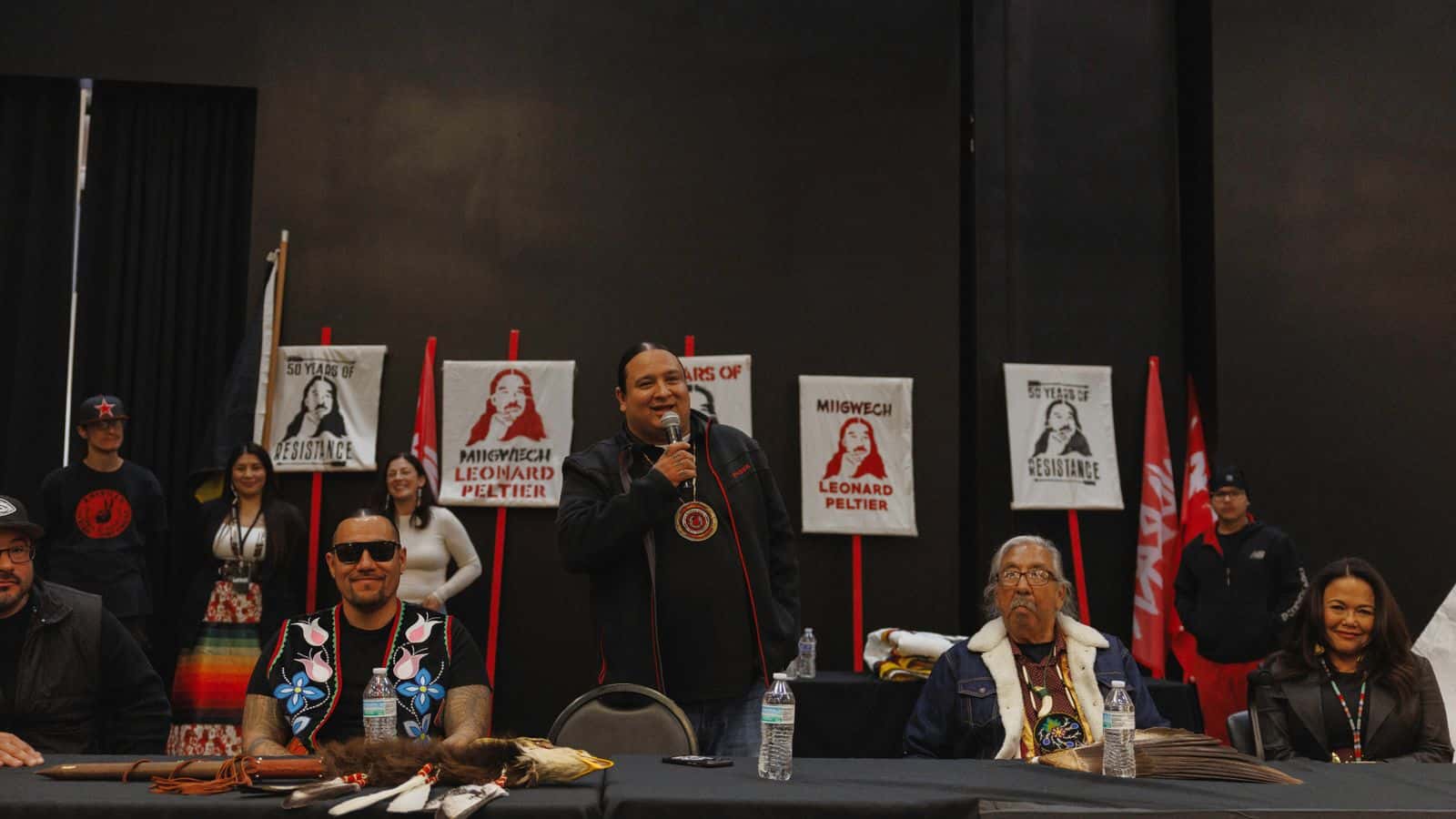 NDN Collective Founder and CEO Nick Tilsen speaks to a crowd at the Sky Dancer Casino in Turtle Mountain, North Dakota after Leonard Peltier (right) was released from prison and subsequently returned home for the first time in 50 years. February 2025. (Photo by Angel White Eyes.)