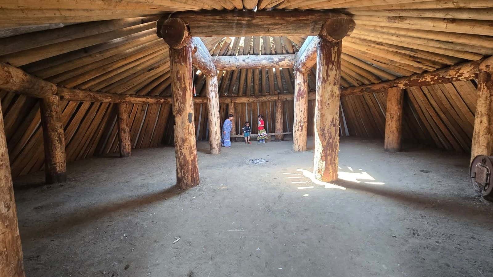 Three kids play inside one of the earthlodges built by Mní Wičhóni Nakíčižiŋ Wóuŋspe students, Bear Soldier, South Dakota, 2021.