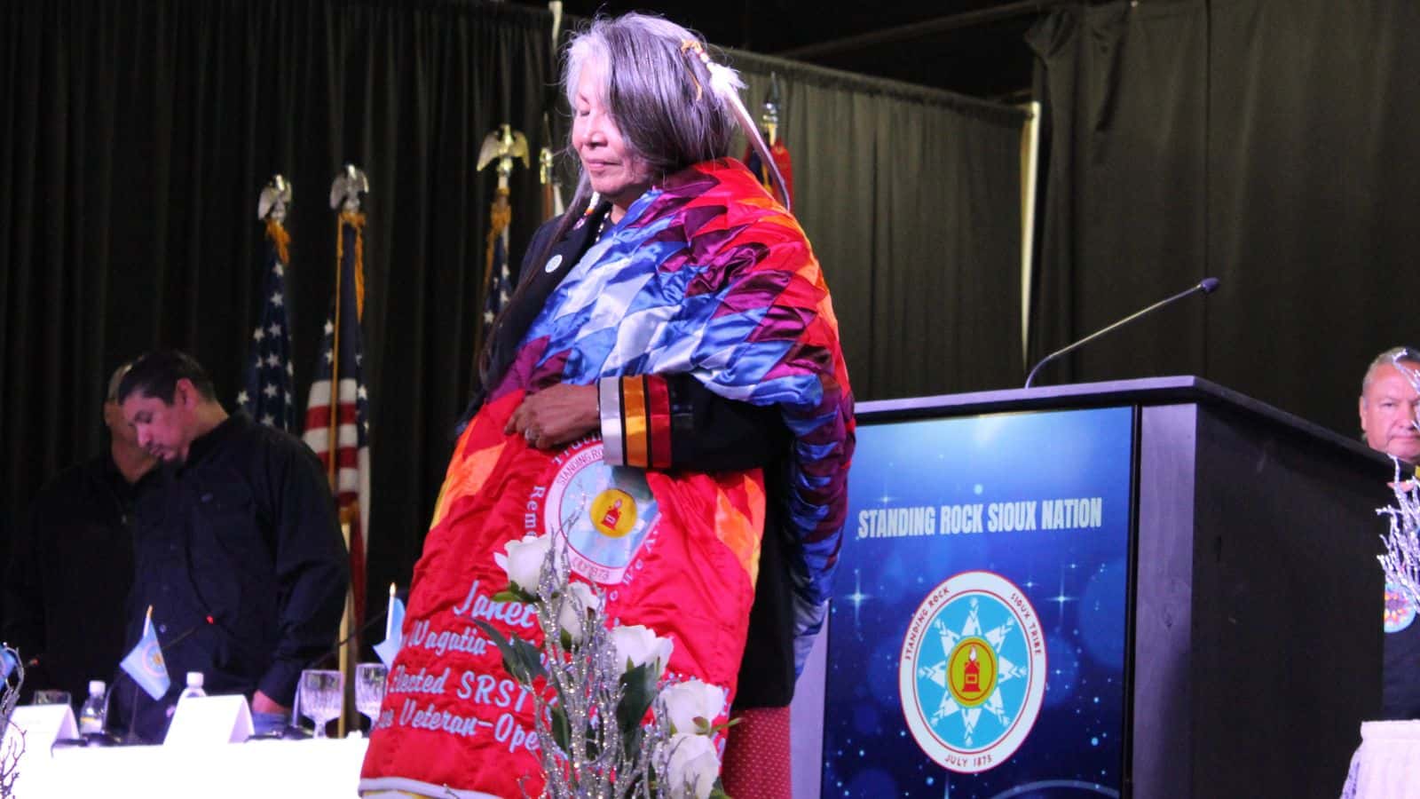 Outgoing Chairwoman Janet Alkire stands on stage with a gifted eagle feather and star quilt at the 2025 Standing Rock Sioux Tribe Inauguration at the Prairie Knights Casino & Resort. Alkire served as chair from 2021 to 2025 and was the first elected woman to hold the position, Fort Yates, North Dakota, Wednesday, Oct. 8, 2025.