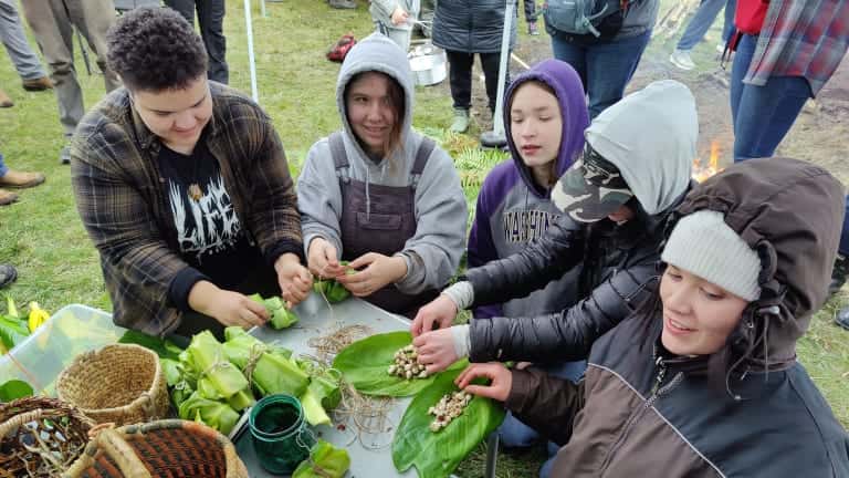 Coast Salish teens and young adults wrap camas bulbs in skunk cabbage to bake in a cooking pit April 15, 2023, during a three-day Indigenous foods event on Whidbey Island in Washington State. (Photo by Richard Arlin Walker for ICT)