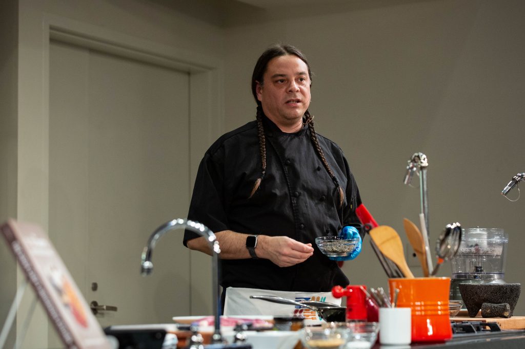 Sean Sherman chef and member of the Oglala Lakota Sioux tribe Indigenous man cooking speaking wearing black clothes and black hair in long braids