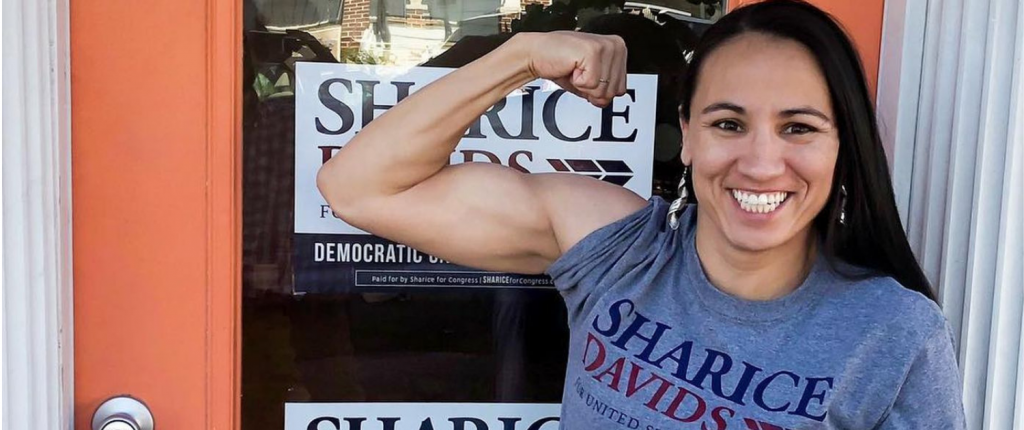 Representative Sharice Davids native american woman flexing her biceps smiling with long hair