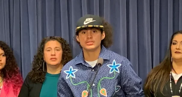 Nimkii Curley, Diné and Ojibwe, center, speaks at a press conference at the Illinois State Capitol on Wednesday, Nov. 16, 2022, at a Native American Summit aimed at drawing attention to Indigenous issues in the state. Curley was not allowed to participate in his graduation ceremony in May 2022 because he had an eagle feather on his graduation cap. Curley's mother, Megan Bang, Ojibwe, second from right in green shirt, also spoke about her son's experience and the harmful effects of Native mascots. The summit was organized by the Chicago American Indian Community Collaborative (Photo by Amelia Schafer for ICT)