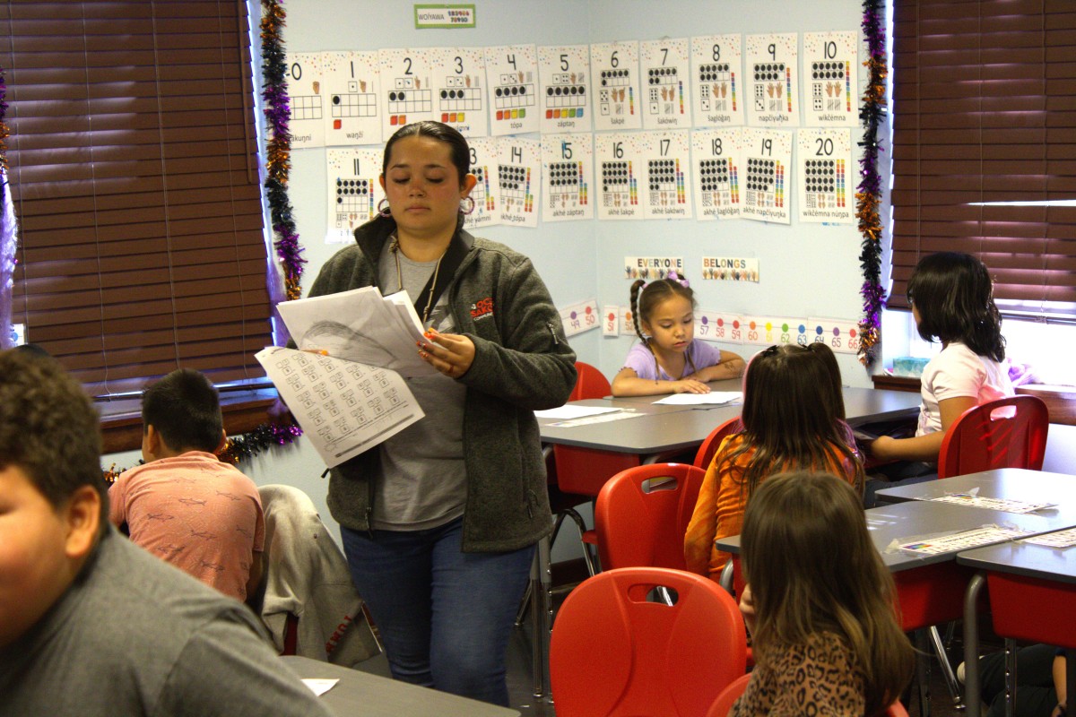 A teacher passes out papers at the Oceti Sakowin Community Academy in Rapid City, where students learn in both Lakota and English. (Photo by Amelia Schafer, ICT/Rapid City Journal)