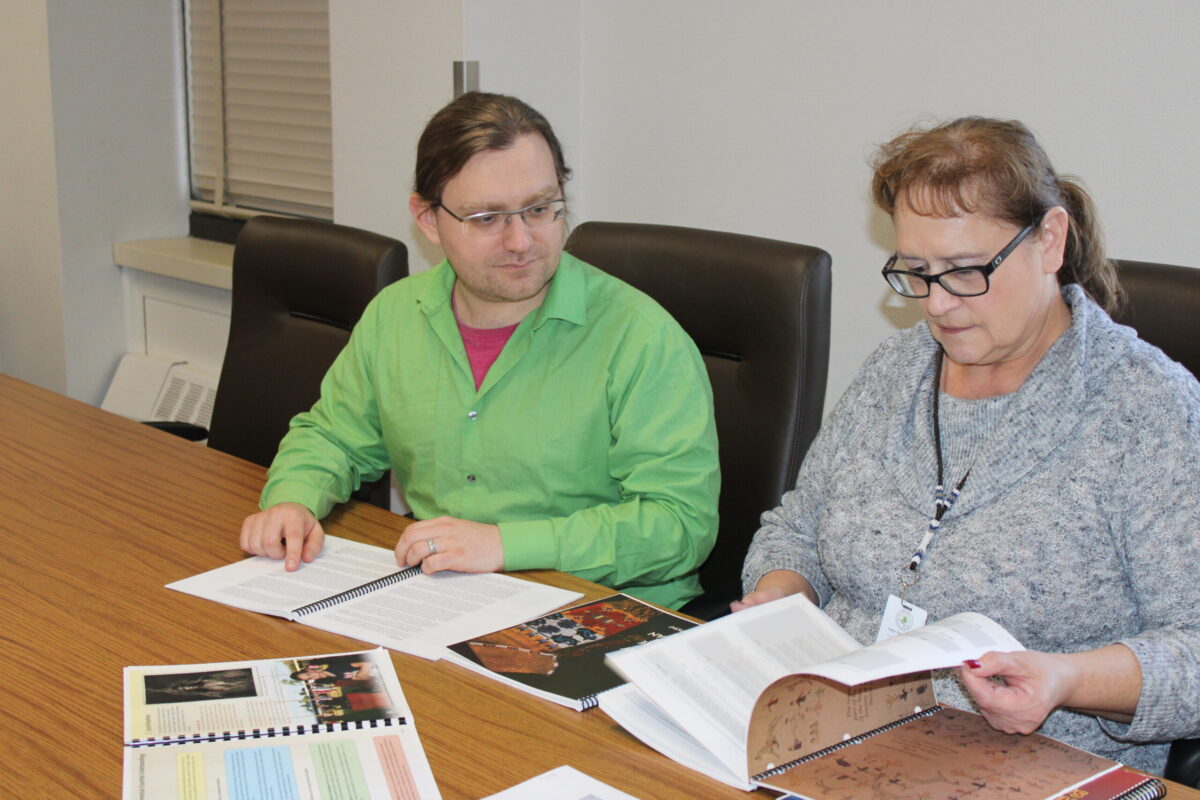 Lucy Fredericks and Nick Asbury peer through the original set of tribal curriculum guides published from 1997 to 2002 to access what other information could be included in the updated versions on Dec. 18. Photo credit/ Adrianna Adame